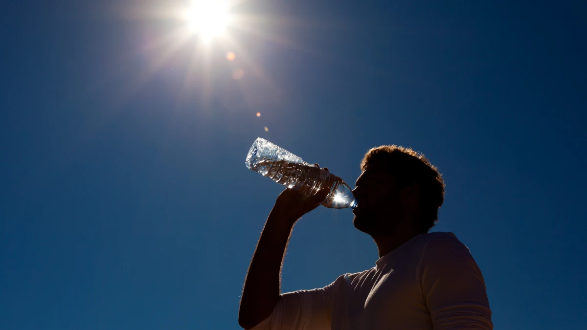 Silhouette eines Mannes trinkt Wasser aus Flasche bei starker Sonneneinstrahlung – Hitzeschutz Neurologie