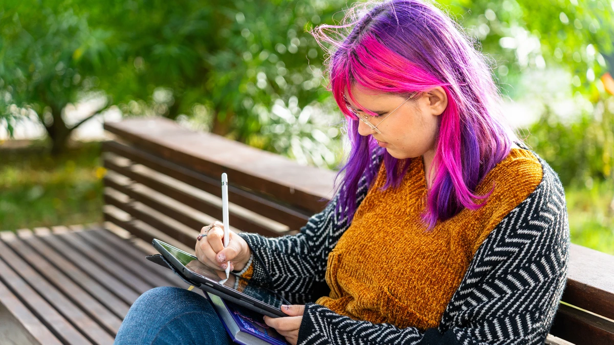 Junge Frau mit pinken Haaren zeichnet auf einem Tablet im Park – Kreativität bei Autismus-Spektrum-Störung