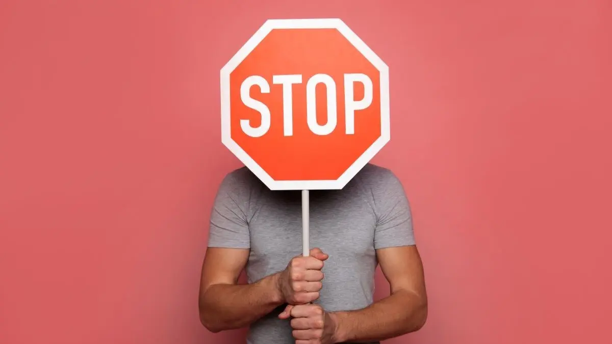 Mann haelt grosses rotes Stoppschild vor dem Gesicht als Symbol dafuer, dass eine schwere chronische Hautentzuendung die Entstehung von Hautkrebs bremsen kann