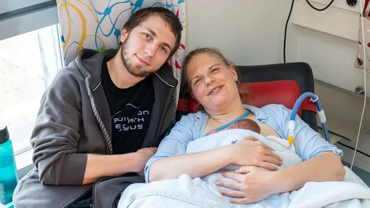 Patientin Vivien F. liegt im Krankenhausbett und hält ihren Neugeborenen Sohn Juda Michael im Arm; Partner Benedikt sitzt lächelnd neben ihr – kurz nach der Geburt am Campus Virchow-Klinikum der Charité trotz schwerer Herzerkrankung der Mutter.